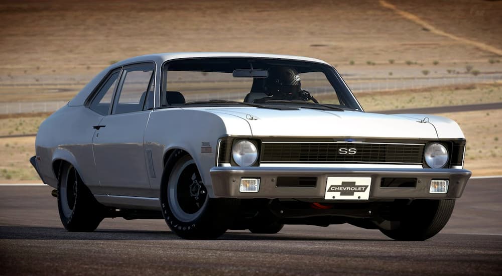 A white 1970 Chevy Nova is on a racetrack. 