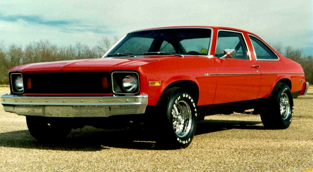 A red 1975 Chevy Nova is parked in a gravely area.