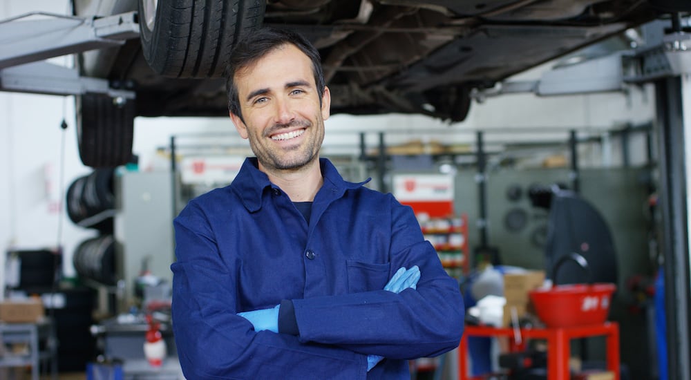 A Smiling mechanic standing in front of an elevated car