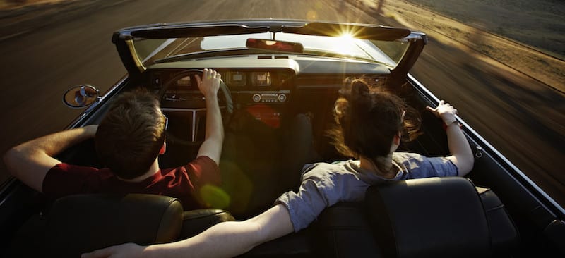 Young couple driving convertible at sunset