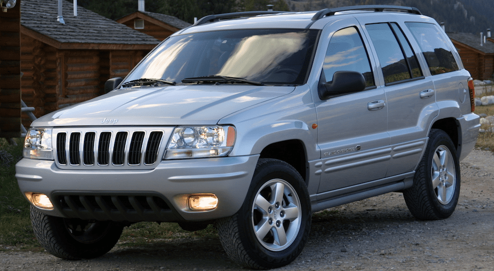 A silver 2001 Jeep Grand Cherokee with a log cabin in back
