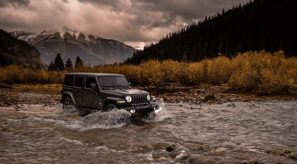 A black 2018 Jeep Wrangler is crossing at river in a mountainous area. You can find used Jeep Wranglers at your local dealer. 