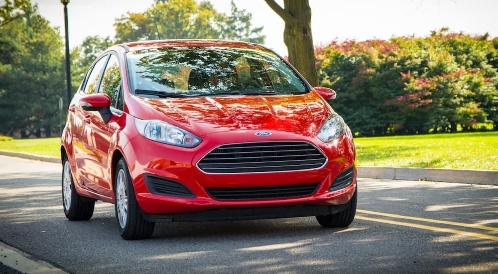 A red 2014 Ford Fiesta, available at some used Ford dealers, is driving along a road with grass and tress behind it.