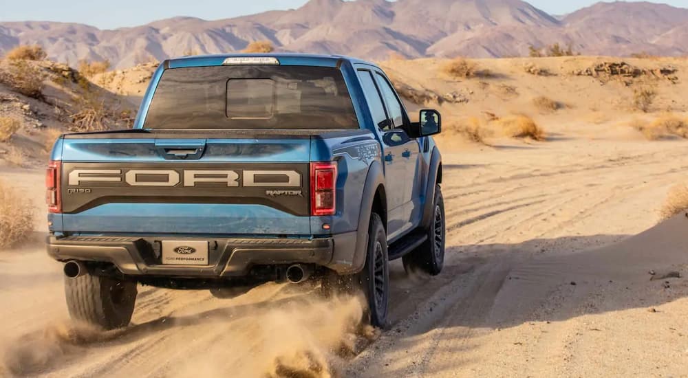 A blue 2019 Ford Raptor from behind, available at Ford dealers, is driving away in the desert.