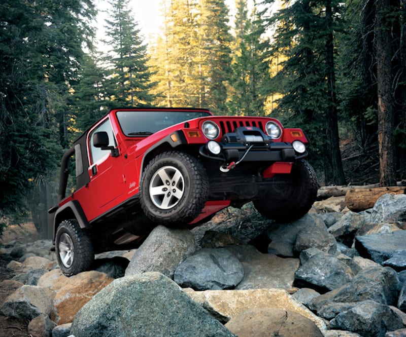 A red used Jeep Wrangler is rock crawling with a winch.