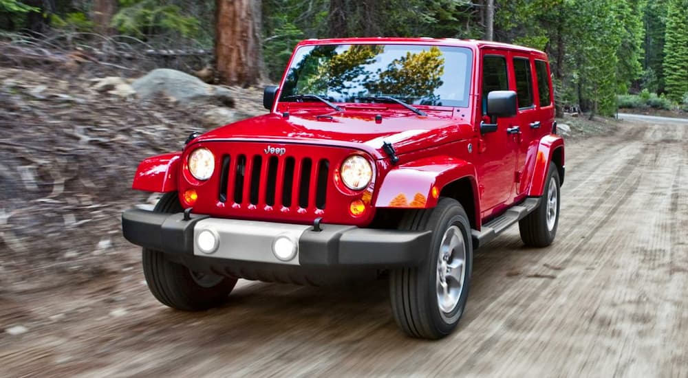 A red 2014 used Jeep Wrangler is driving through the woods on a dirt road.