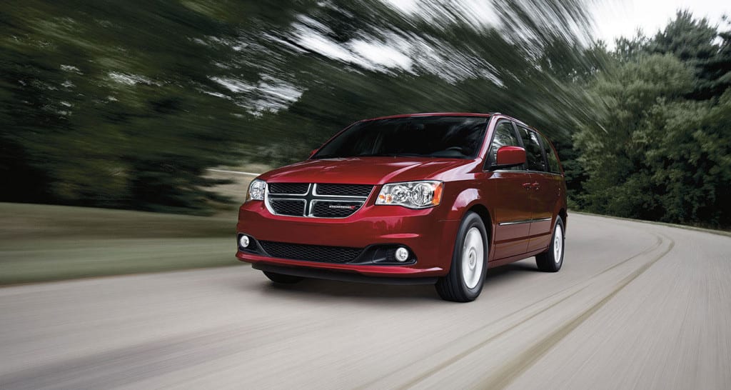 A red 2015 Dodge Grand Caravan is driving around a corner on a rural road.