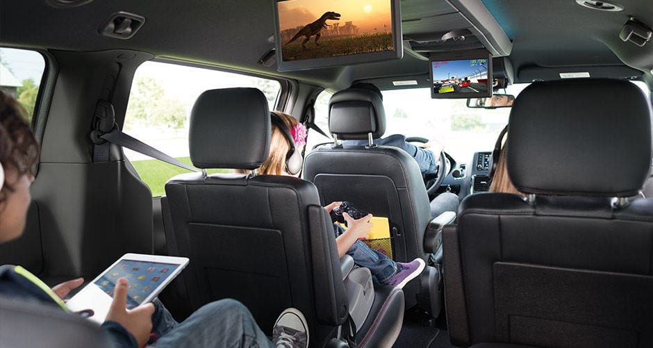 Kids in the back of a 2016 Dodge Grand Caravan are using the built in monitors.