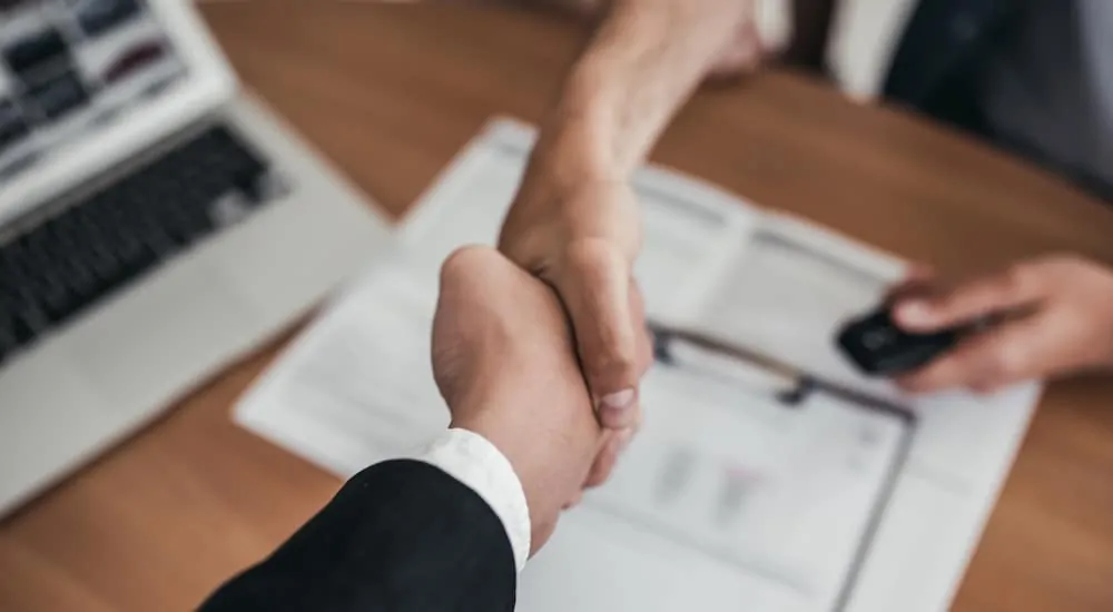 Two hands shaking over car purchase paperwork