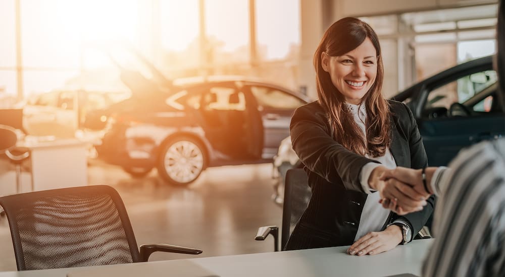 Woman sitting at white table in car dealership shaking hands