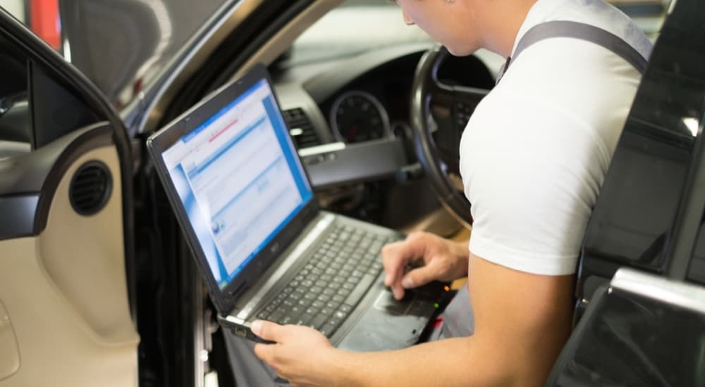 A mechanic is checking the OBD2 readings on his laptoip in a car to give a car repair estimate.