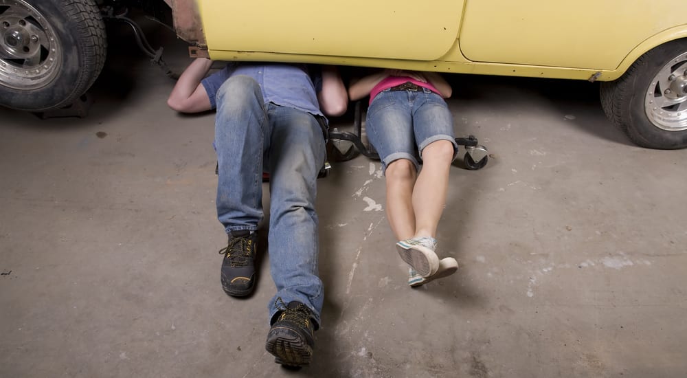 A man and woman working under a car together with their legs sticking out.