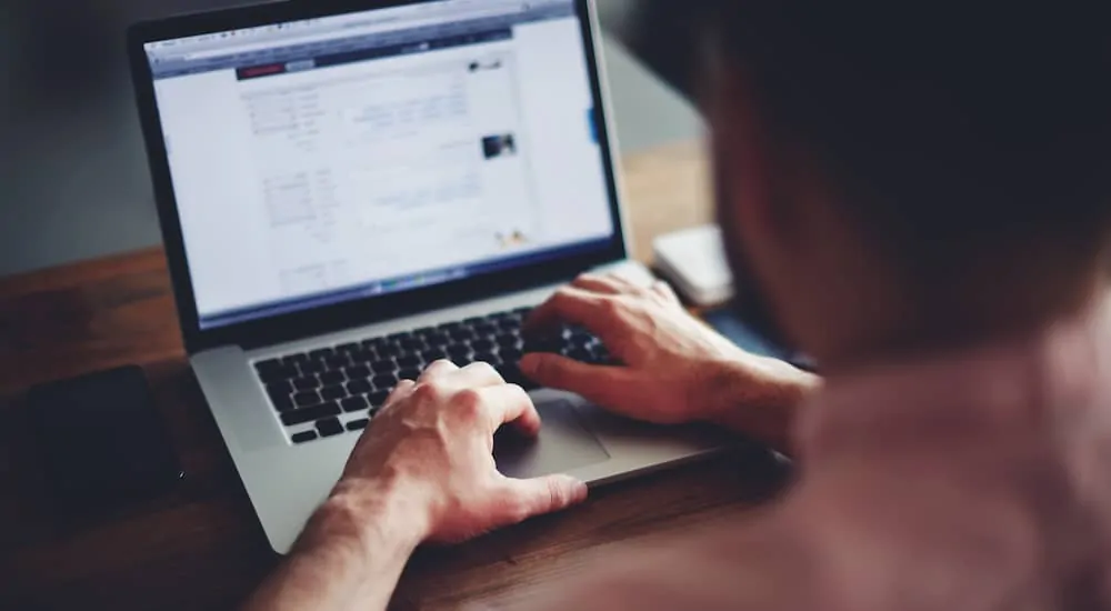 A man using his laptop for research on a wooden table