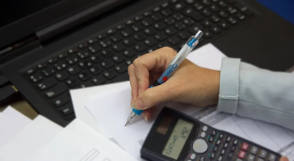 A laptop with notes on top of it being written on by a woman with a pen