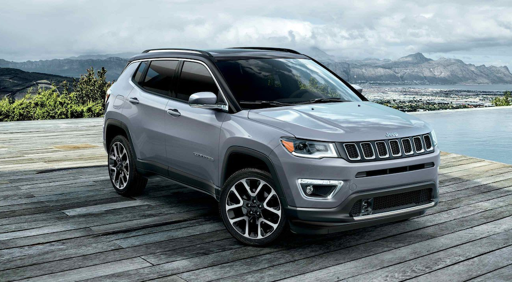 A 2019 grey Jeep Compass is parked on a high platform with tropical bay views. 