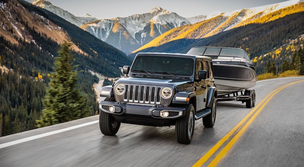 A black Wrangler tows a boat along a mountain road, the joys you can have from a Jeep dealership near you!