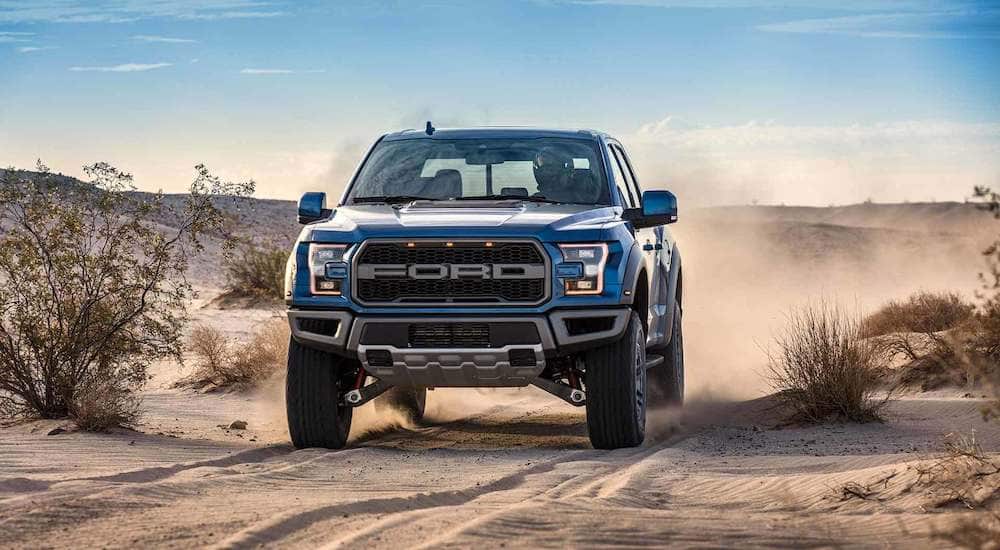 A blue 2019 Ford Raptor races across a desert landscape