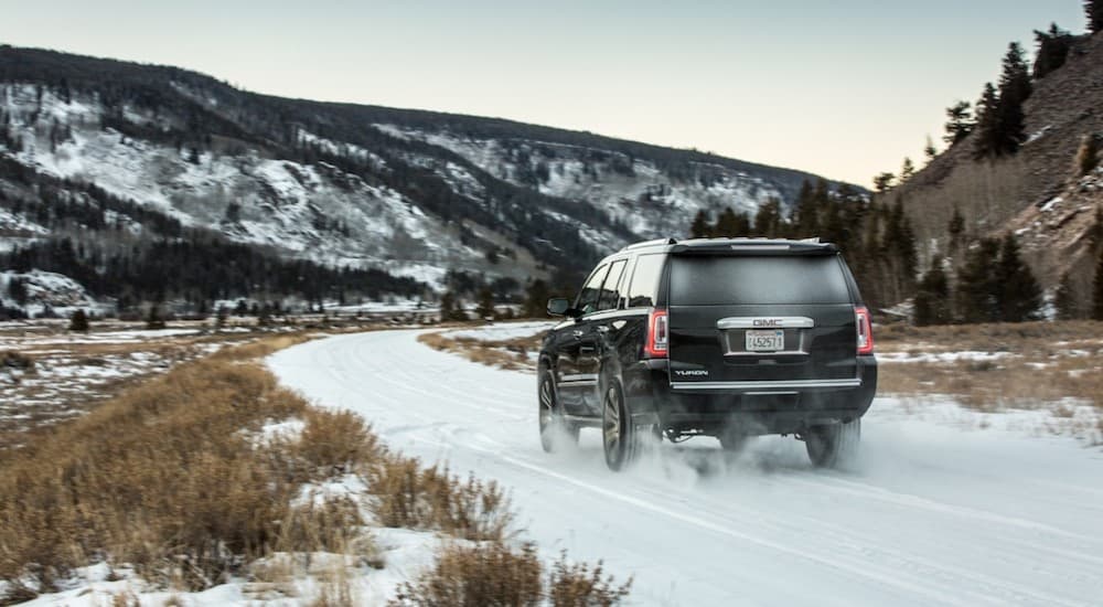 The back end of a 2019 GMC Yukon Denali as it drives into the snowy mountain sunset