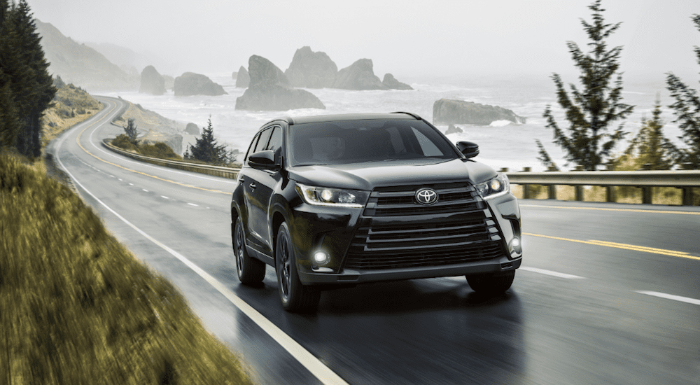 A black 2019 Toyota Highlander travels a rainy coastal highway