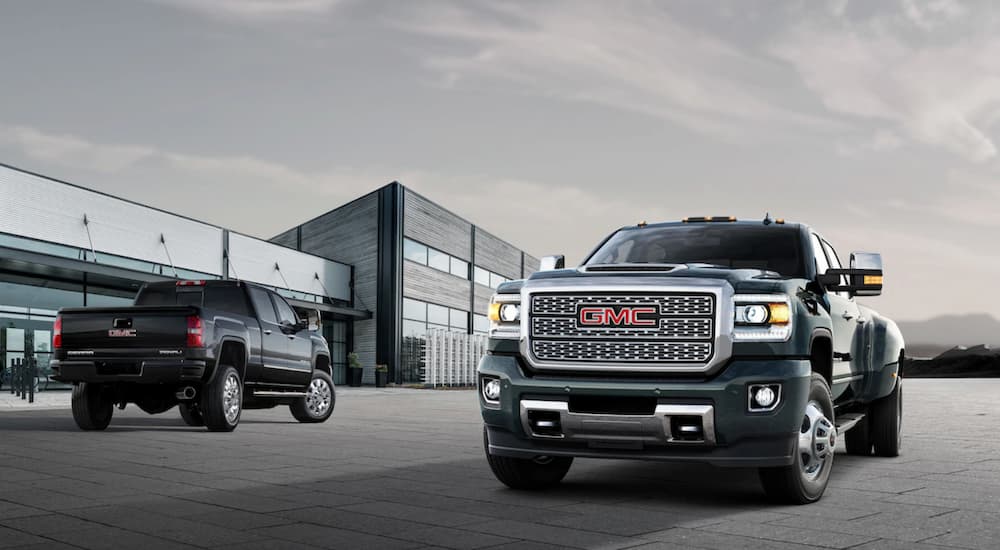 Black 2019 GMC Sierra 3500HD Denali and 2500HD trucks in front of wood, metal and glass building
