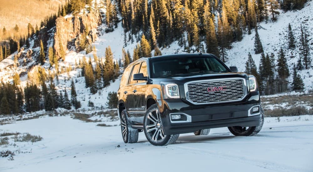 Black 2019 GMC Yukon Denali driving on snow covered road in mountains