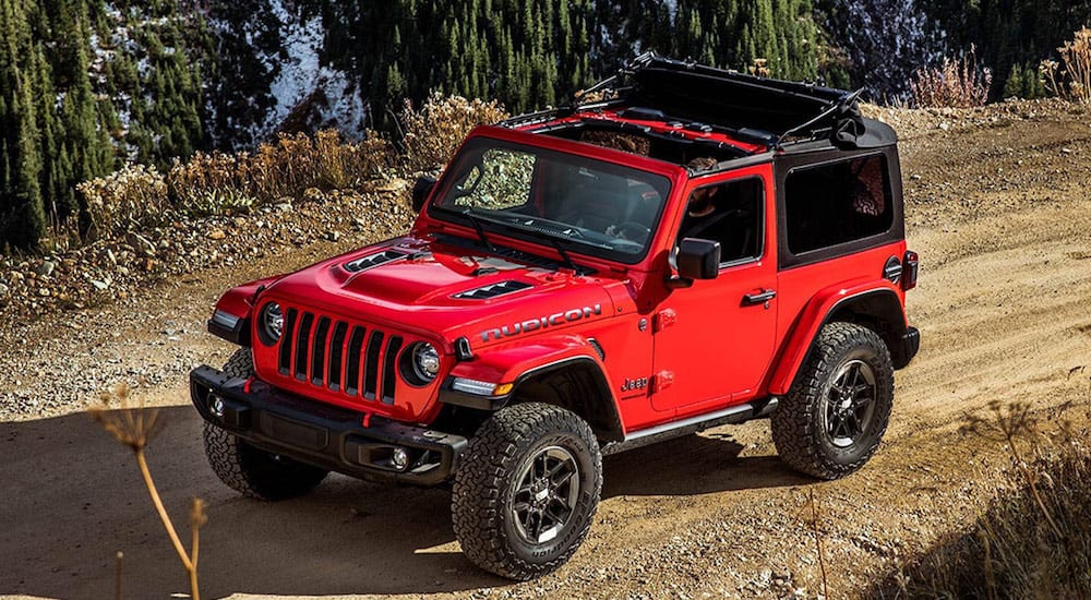 A red 2019 Jeep Wrangler with the top open drives a tight dirt road