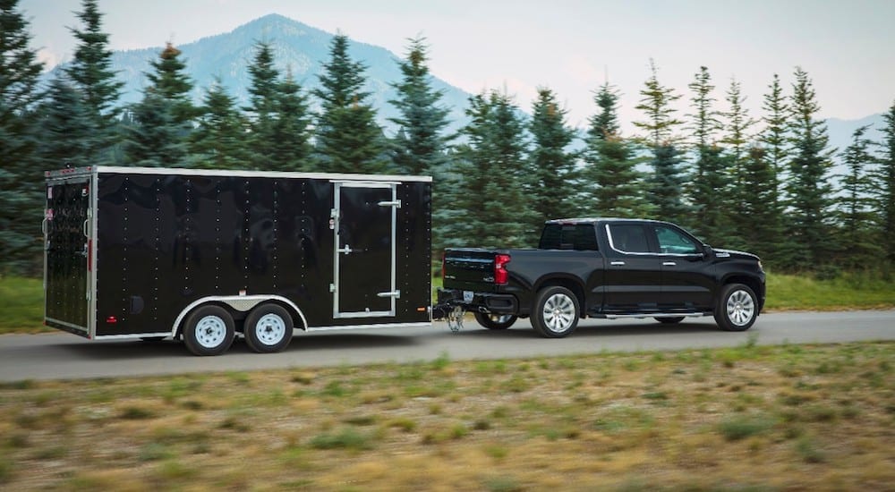 A black 2019 Chevy Silverado High Country towing a black trailer with trees and mountain in back