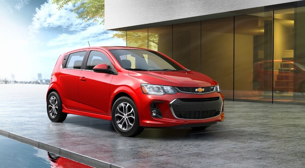 A red 2019 Chevy Sonic hatchback parked in front of a modern building