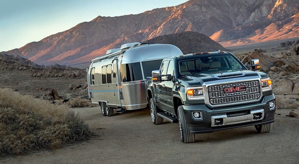 A black 2019 GMC Sierra 2500HD Denali towing a trailer in the desert with mountains in back