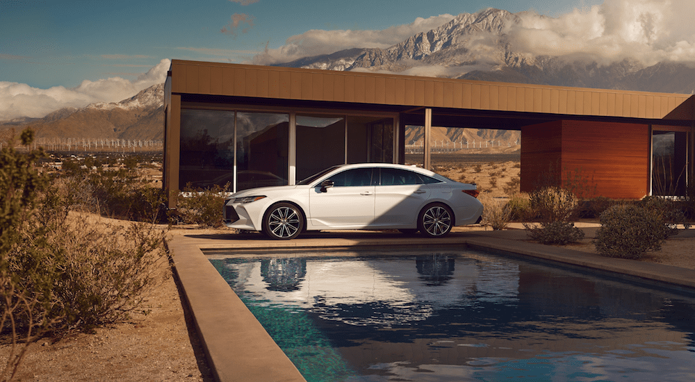 A white 2019 Toyota Avalon at a desert mansion with pool and wind turbines