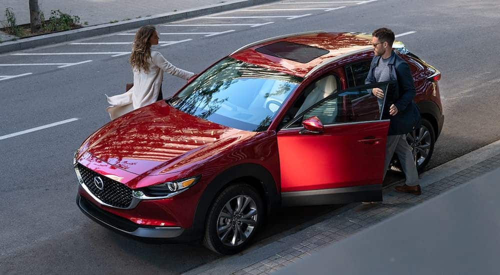 A smiling couple is getting into their red 2020 CX-30 that's parked on a street. 