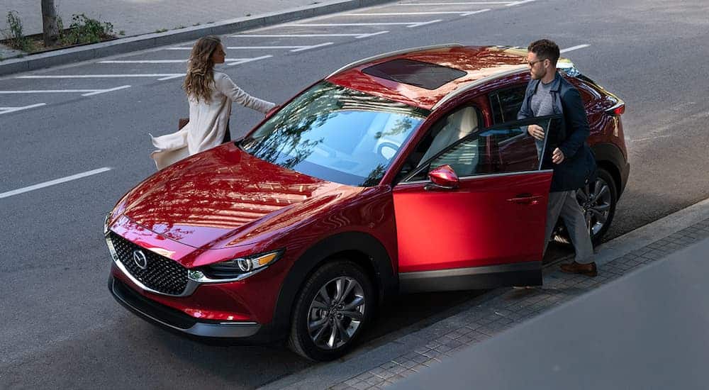 A smiling couple is getting into their red 2020 CX-30 that's parked on a street. 