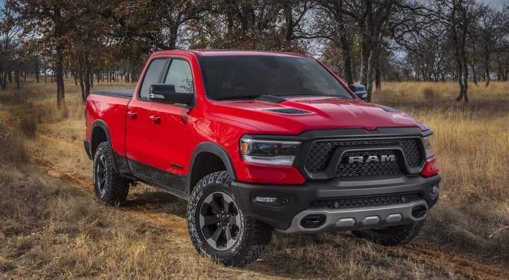 A red 2020 Ram 1500 Rebel is parked on a dirt trail with trees in the distance. 