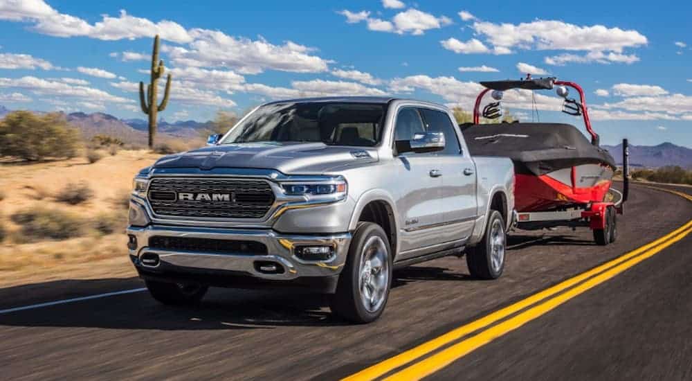 A silver 2020 Ram 1500 is towing a large boat against a vibrant blue and cloudy sky.
