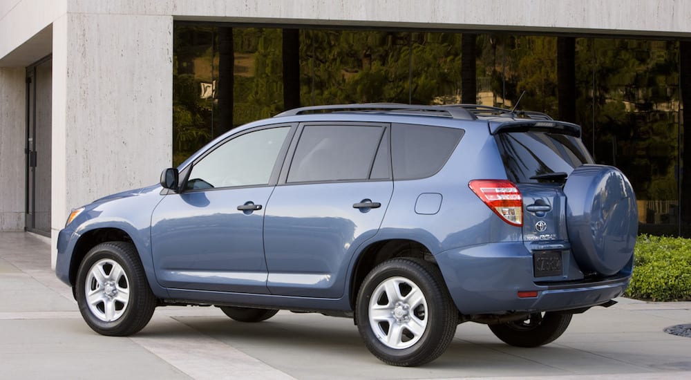 A blue RAV4 from a local used car dealer outside a concrete and glass home