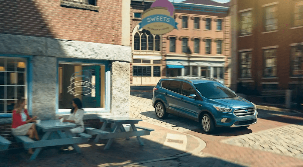 A blue 2019 Ford Escape drives past a city candy store