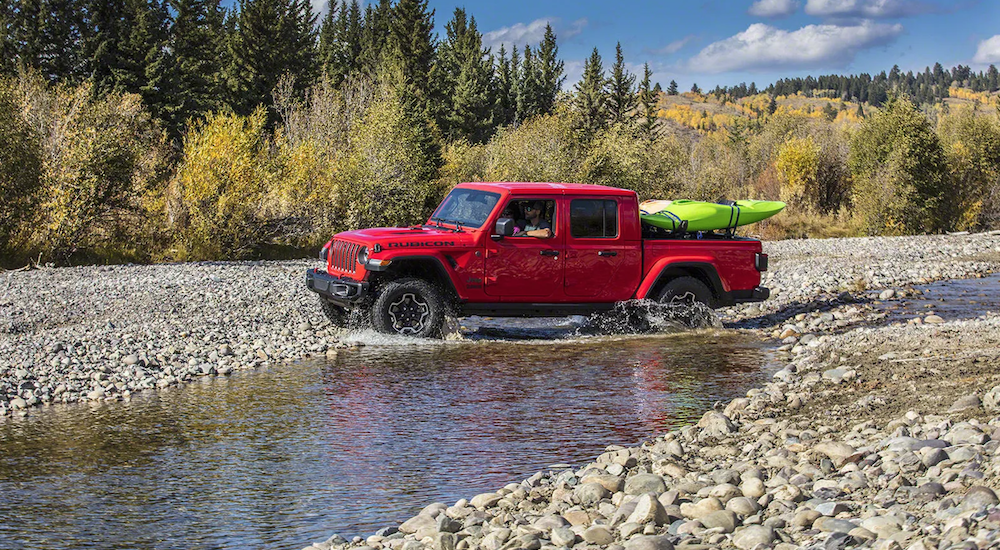 A red 2020 Jeep Gladiator crosses a river with kayaks in the bed