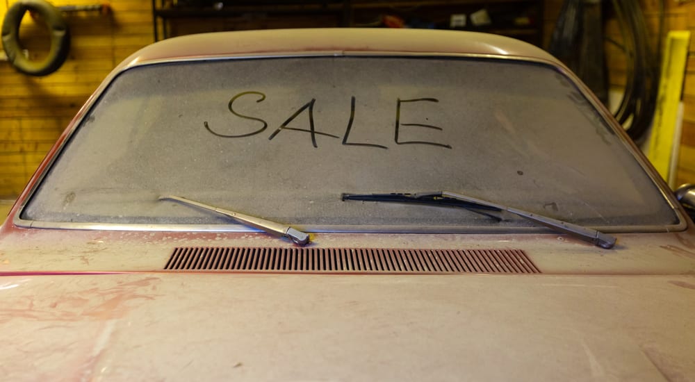 A dusty car in a garage with 'sale' written on the windshield. A poor quality vehicle is the sign you are at the wrong jeep dealership
