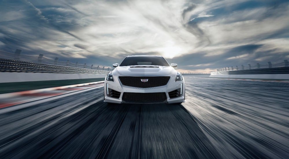 A white 2019 Cadillac CTS-V from the front racing around a track in front of a cloudy blue sky