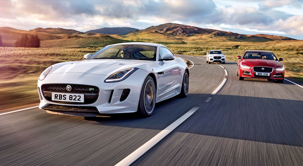 Two white and one red Jaguar models are driving in the sunshine.