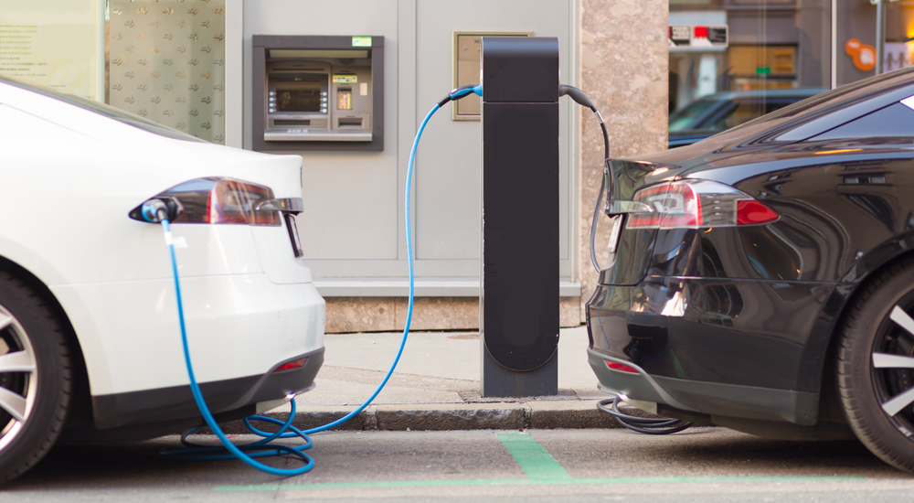 A black sedan and a white sedan are charging at an electric car station.