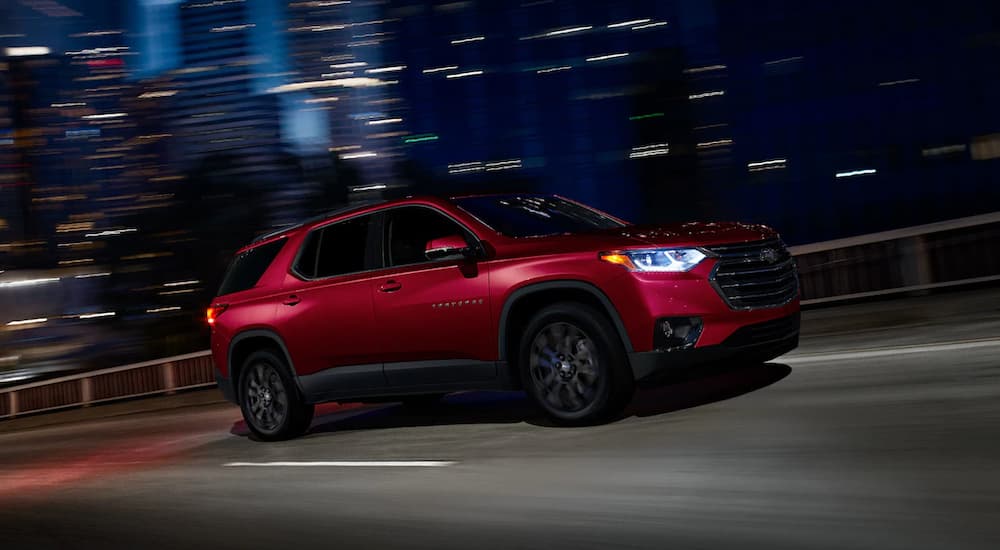 A red 2019 Chevy Traverse with black trim is driving at night with blurry buildings behind it. Look at the V6 model perfomance when comparing the 2019 Chevy Traverse vs 2019 Dodge Durango.