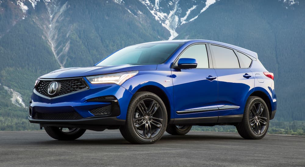 A blue 2019 Acura RDX is parked in front of mountains. In automotive news, it won “Best Luxury Compact SUV for Families”.