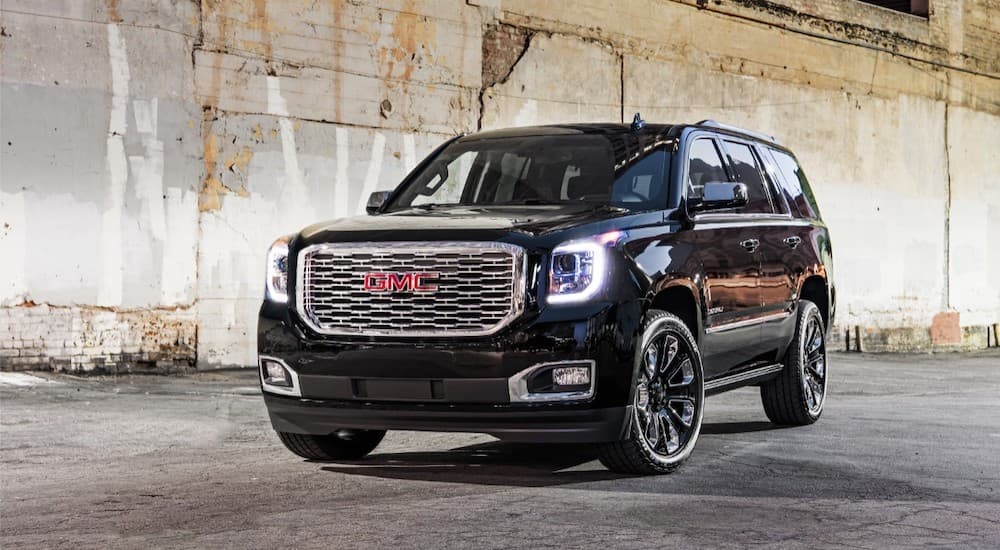 A black 2019 GMC Denali is parked in front of a crumbling wall. It is in the lineup of GMC SUVs.