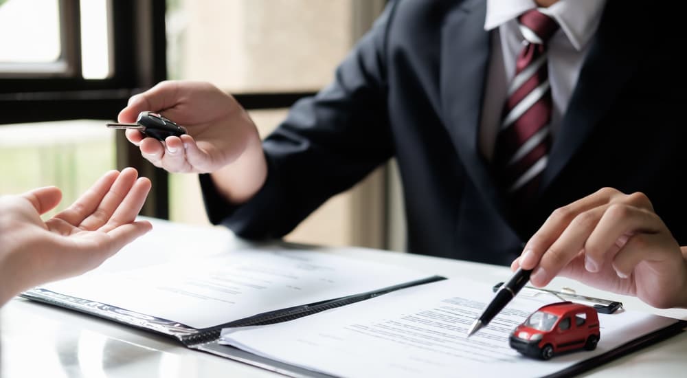 A dealer is handing over the keys with the financing paperwork under his arm.