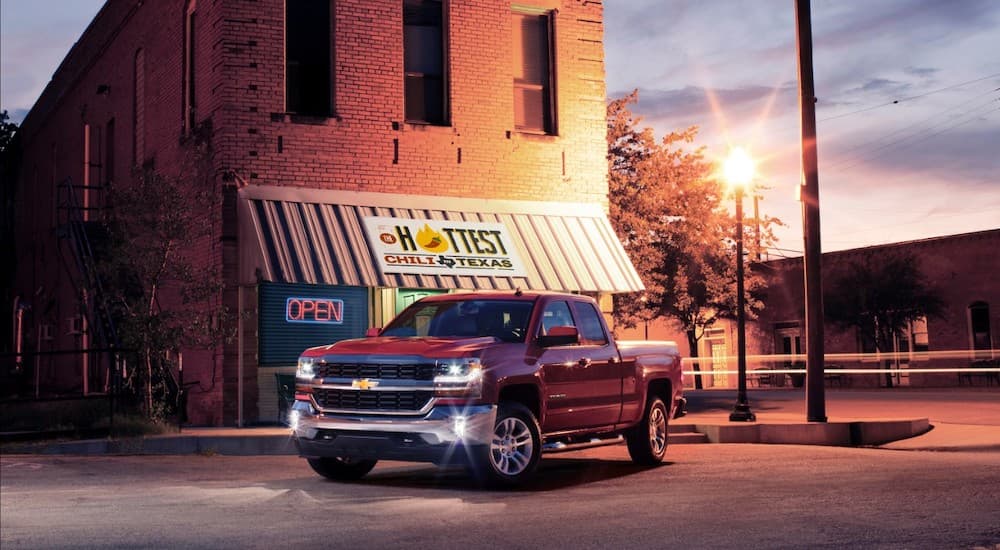 A red 2016 Chevy Silverado 1500 is parked outside of a brick restaurant at night.
