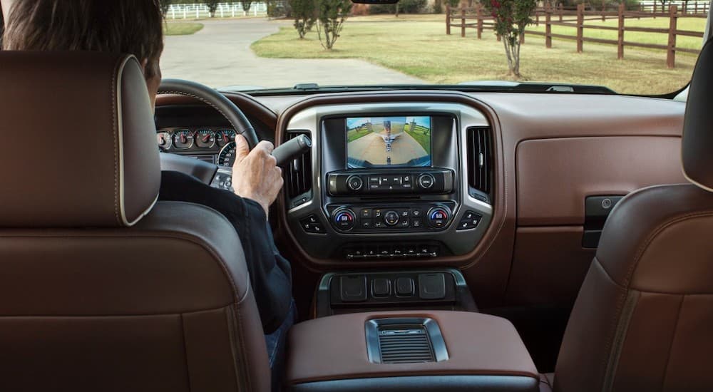 The brown interior of a 2017 Chevy Silverado 1500 is shown with a man driving. He is testing the reverse camera on a used Chevy Silverado for sale.