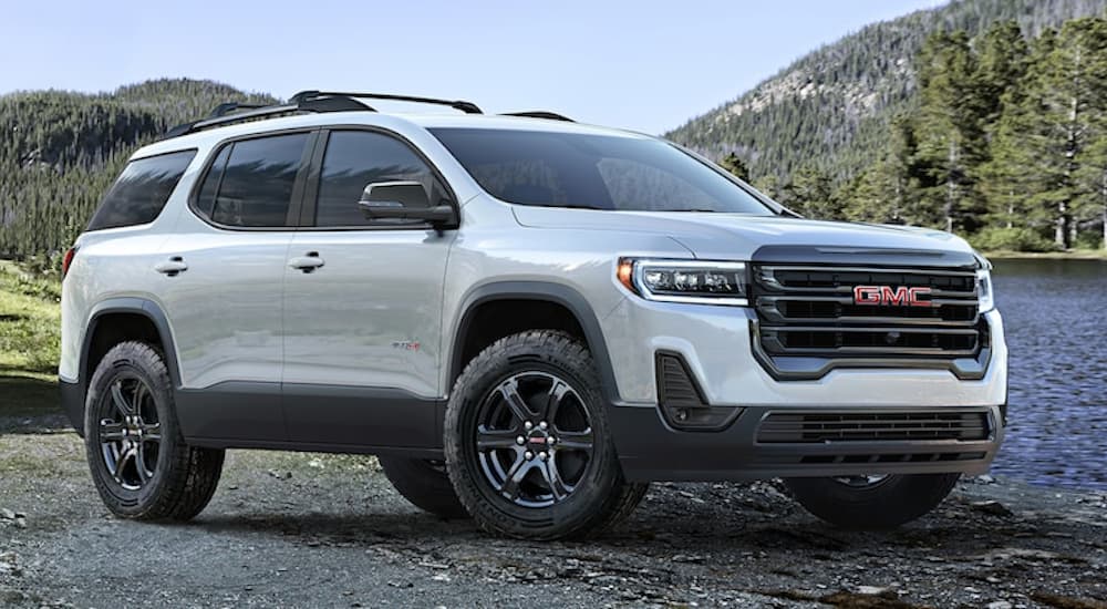A white 2020 GMC Acadia is shown in front of a lake and trees.