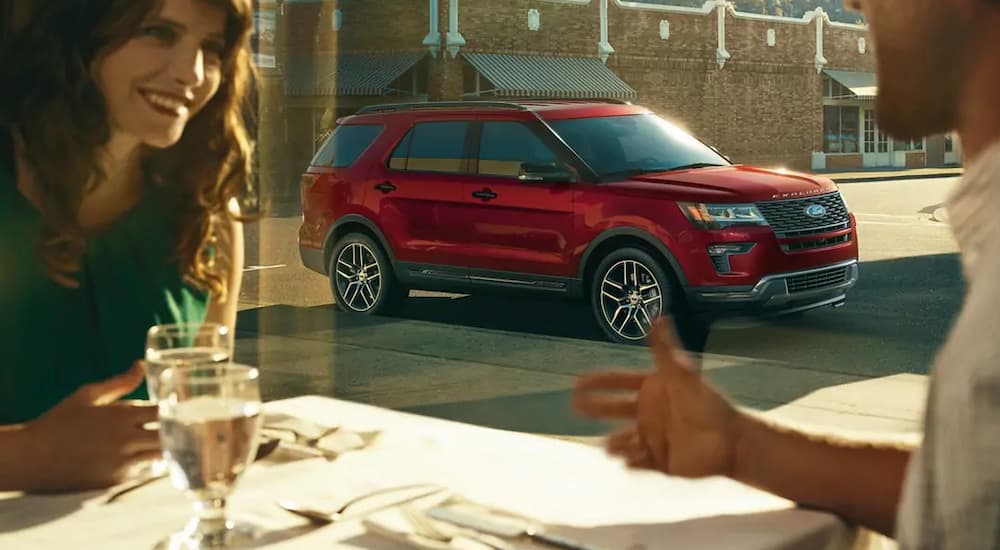 A red 2019 Ford Explorer can be seen through the window of a restaurant while a couple eats. Check out safety when comparing the 2019 Ford Explorer vs 2019 Honda Pilot.