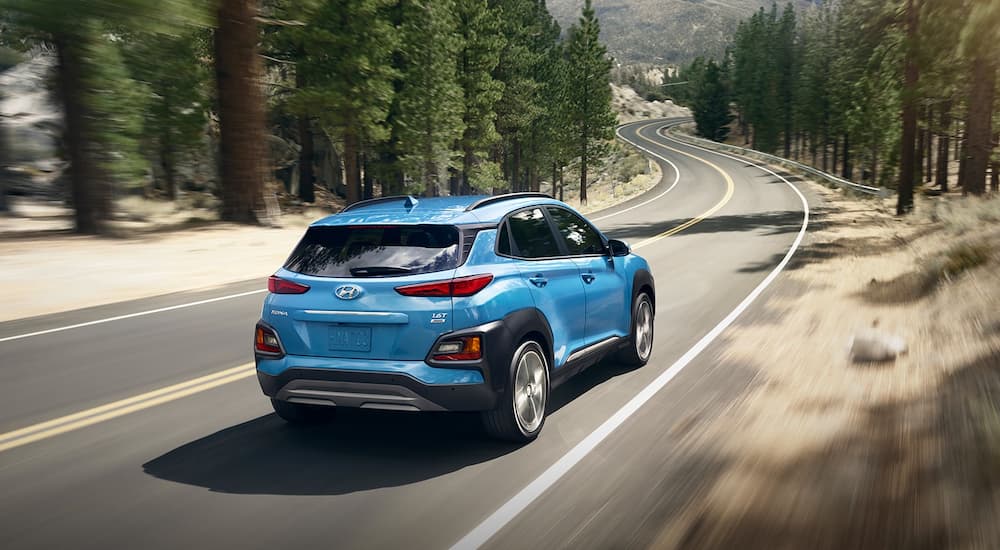 A blue 2019 Hyundai Kona is driving along a windy tree-lined road.